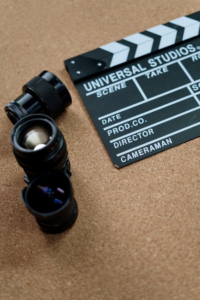 Flat lay of vintage film equipment including lenses and clapboard on cork surface.