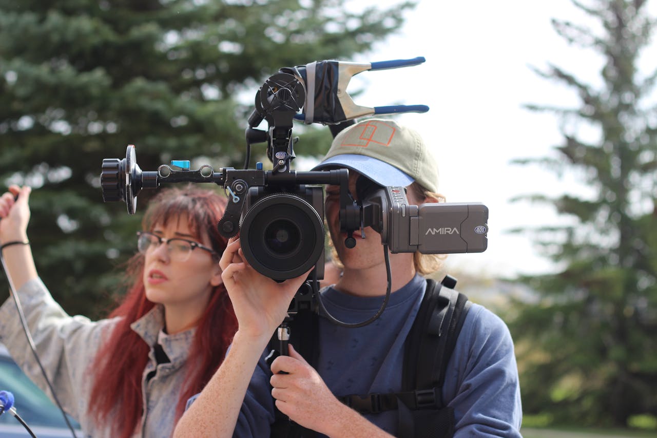 Two filmmakers operate a high-end Arri Amira camera in a natural setting, capturing outdoor scenes.